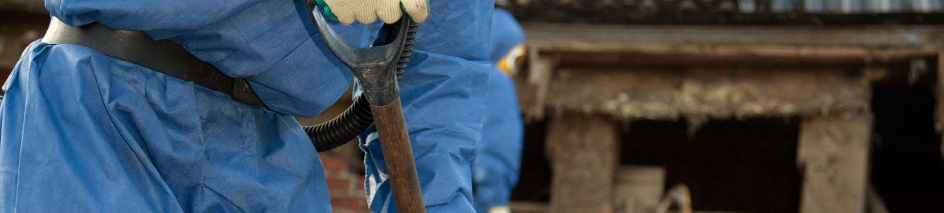 Das Bild zeigt einen Arbeiter mit Sachkunde Asbest in Schutzkleider, der einen Spaten hält und arbeitet.