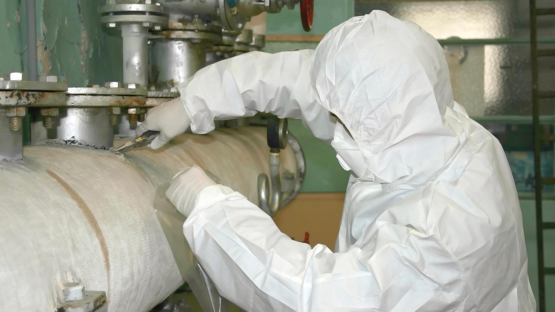 Das Bild zeigt einen Arbeiter in Schutzkleidung bei der Asbestsanierung von Rohr-Isolierungen